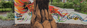 A sculpture made from wood with a colourful banner that reads Phoenix Gardens